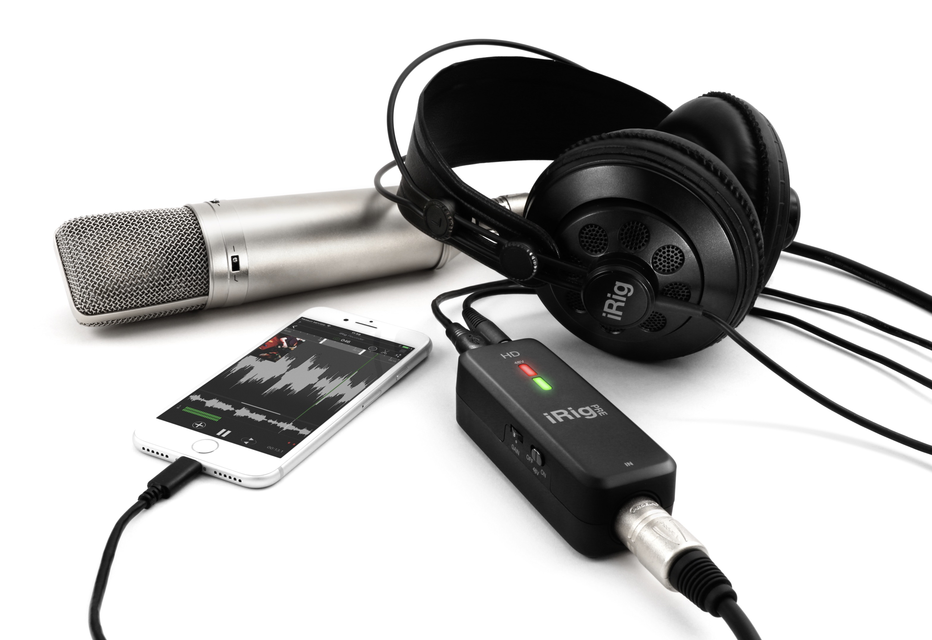 Microfono argentato, smartphone, interfaccia audio nera e cuffie su bianco.