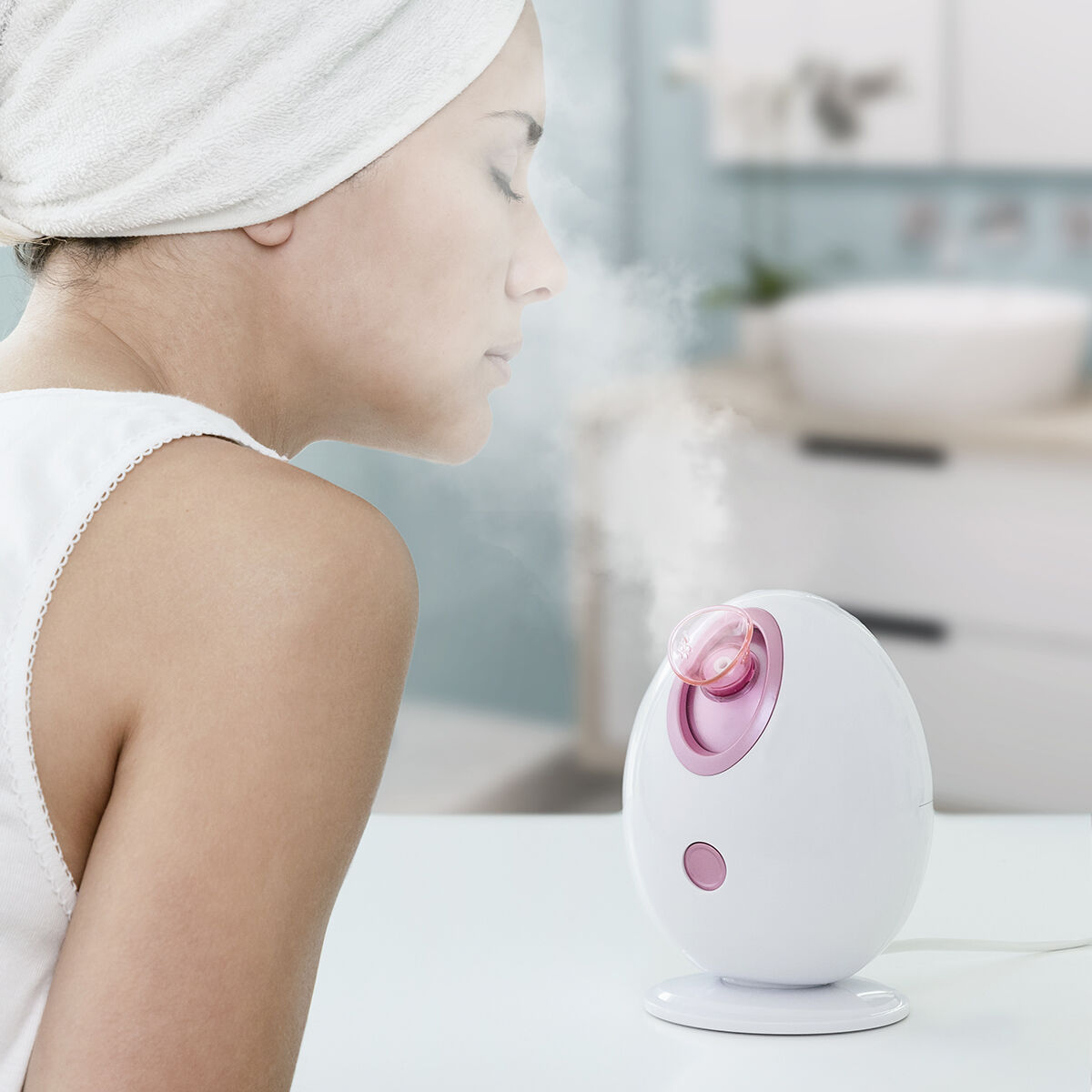 Una donna con asciugamano in testa inala vapore da un vaporizzatore per il viso.