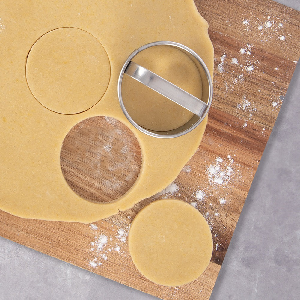 Un cortador de galletas redondo corta círculos de masa amarilla en una tabla de madera.