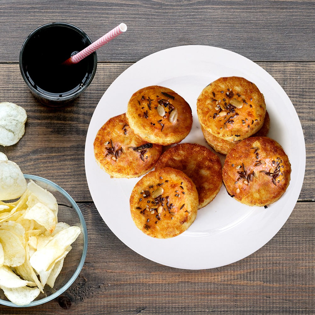 Galletas redondas, doradas y espolvoreadas con semillas en un plato, junto a un vaso de bebida oscura y patatas fritas.