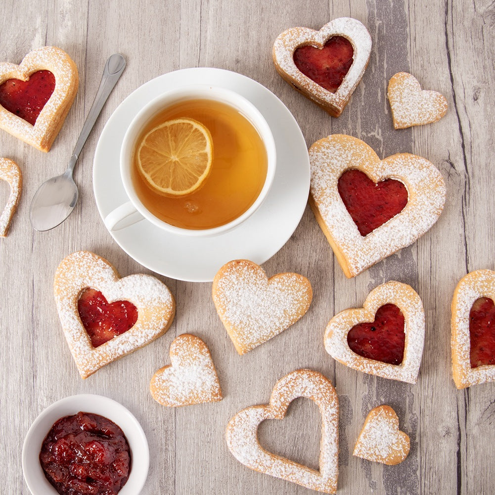 Galletas en forma de corazón con mermelada y azúcar glas, servidas con té.