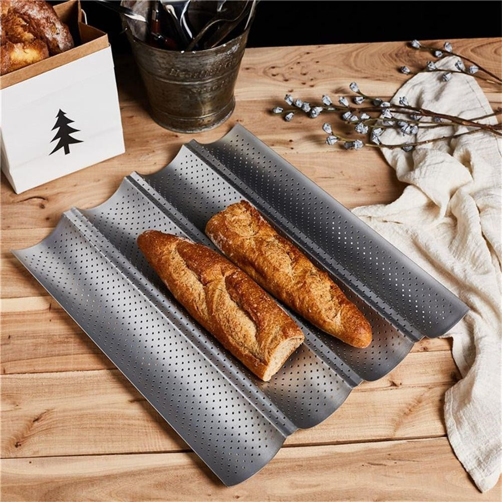 Dos baguettes en una bandeja para hornear perforada sobre mesa.