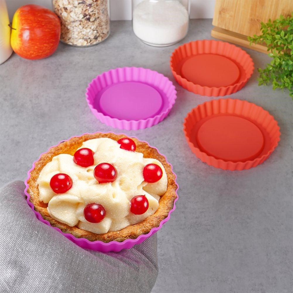 Una tarta en molde morado cubierta de bayas. Dos moldes naranjas cerca.