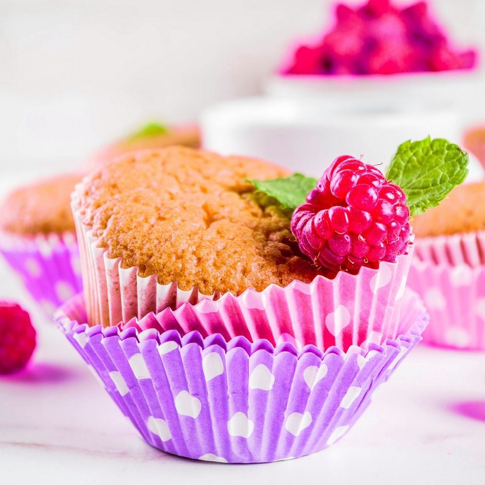 Un muffin en moldes de cupcake morados y rosas con lunares, con frambuesa y menta.