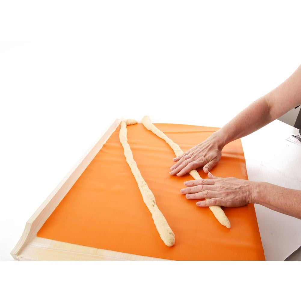 Manos trenzando tres hebras de masa sobre tapete naranja.