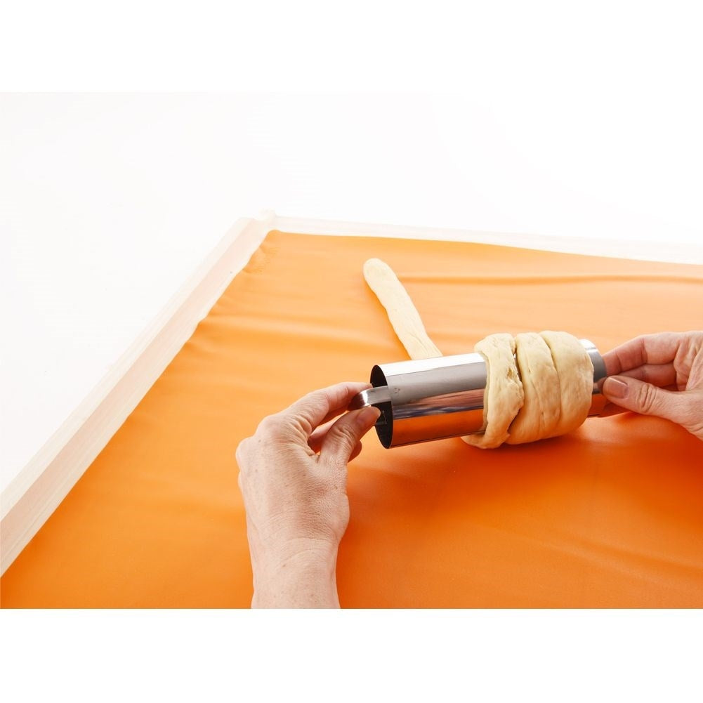Manos dando forma a la masa alrededor de un tubo metálico sobre una alfombrilla naranja.