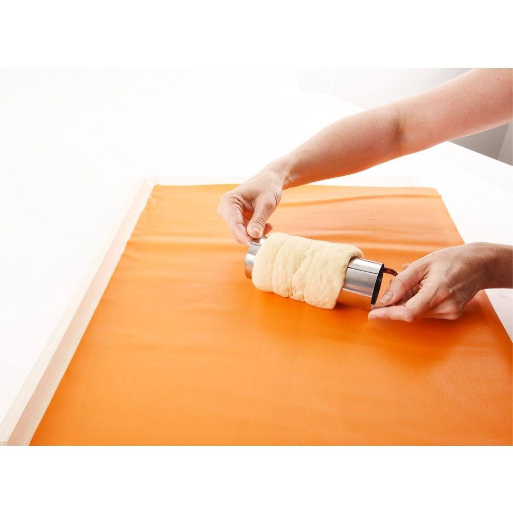 Manos dando forma a la masa alrededor de un tubo de metal sobre una alfombrilla naranja.