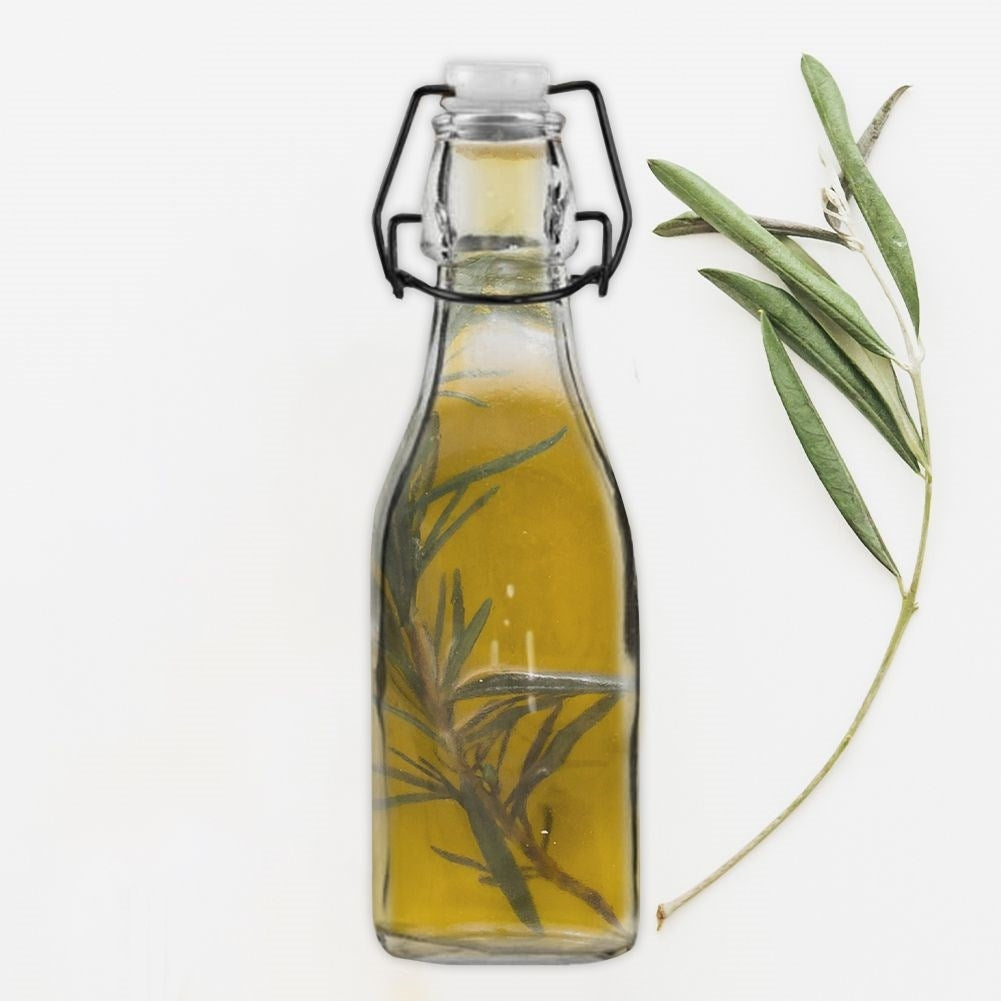 Botella de vidrio con aceite amarillo y ramita de romero, junto a una ramita de olivo.