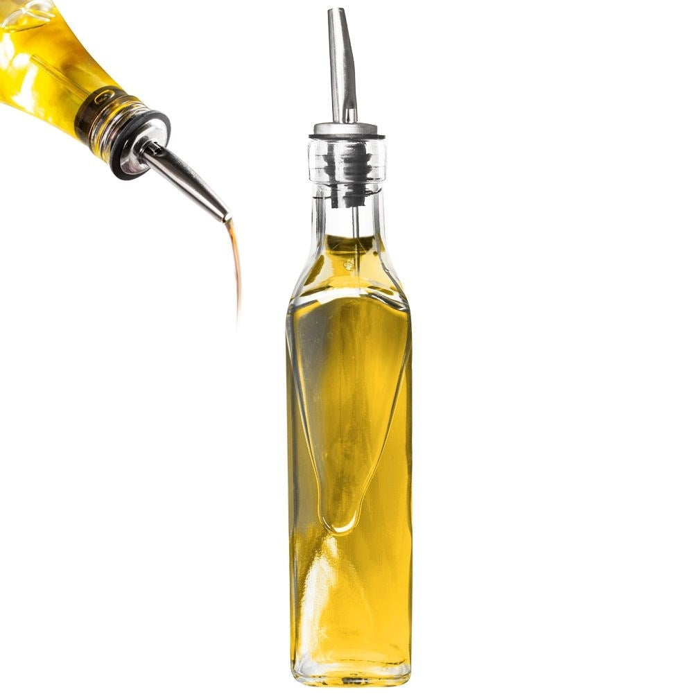 Botella de aceite de vidrio con un vertedor plateado, goteando aceite.