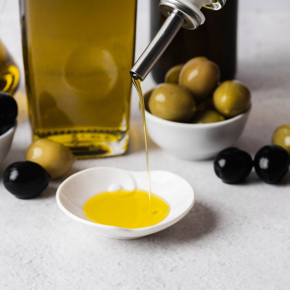 El aceite de oliva fluye de un vertedor a un plato; aceitunas verdes y negras cerca.
