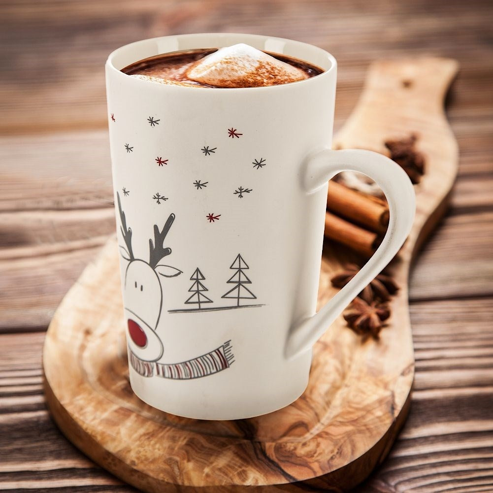 Una taza blanca con chocolate caliente y malvaviscos, decorada con un reno.