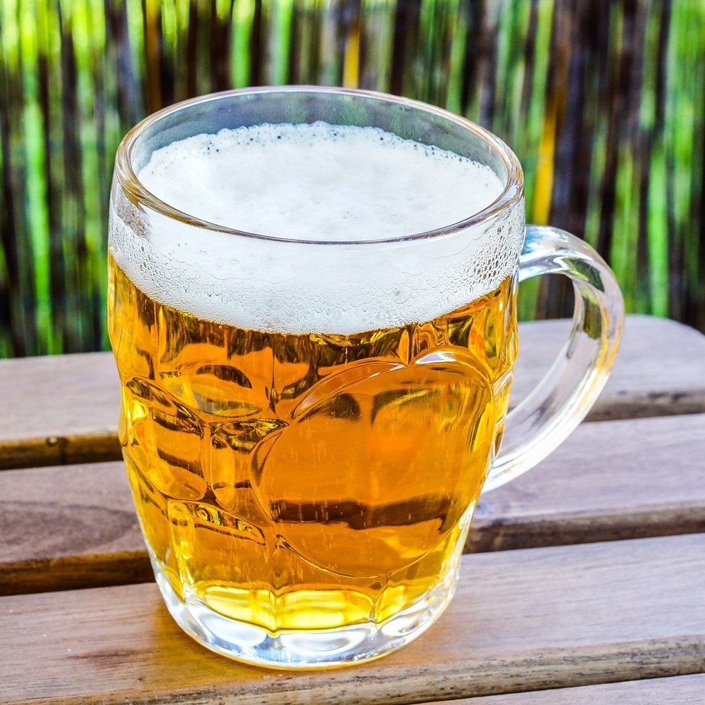 Una jarra de cerveza con espuma sobre una mesa de madera, con fondo verde.