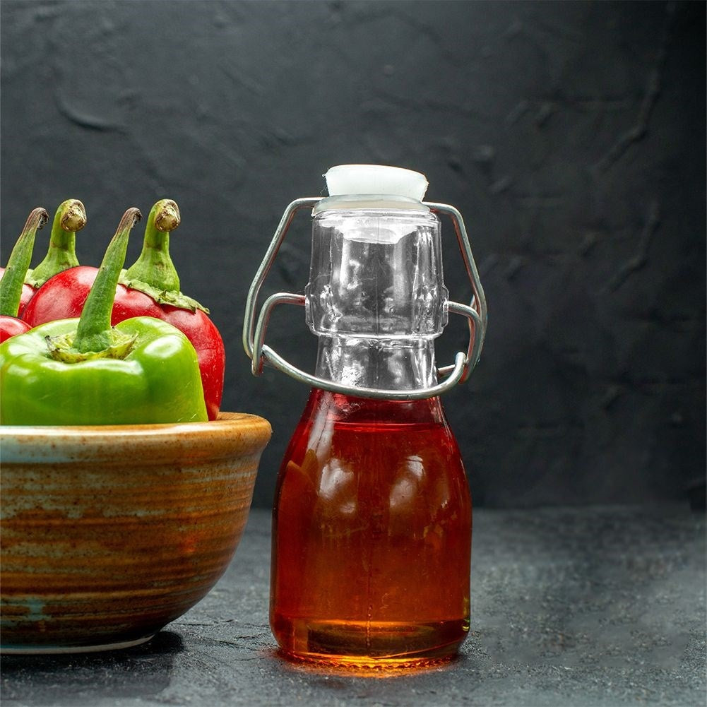 Pimientos verdes y rojos en un cuenco junto a una botella de cristal con líquido rojo.