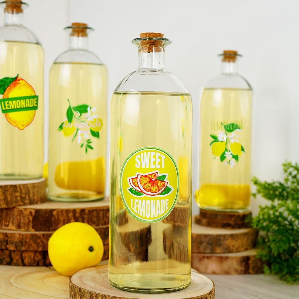 Cuatro botellas de limonada amarilla, decoradas con cítricos y etiquetas.