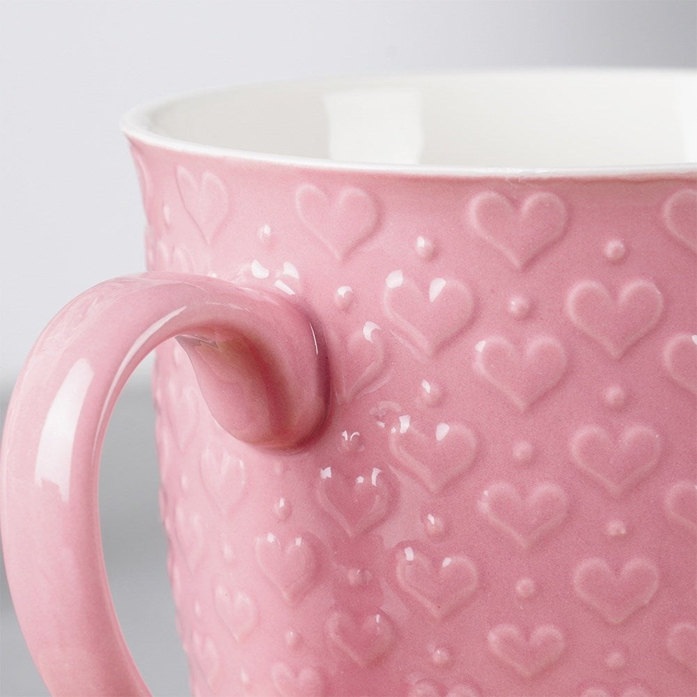 Primer plano de una taza rosa con patrón de corazón y borde blanco.
