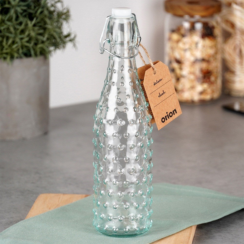 Botella de vidrio transparente con relieve y cierre abatible, con etiqueta.