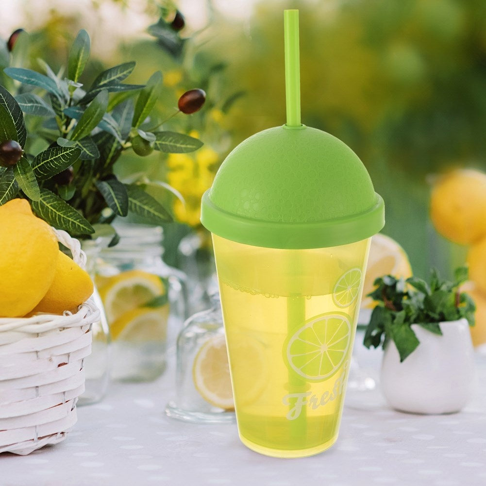Una taza amarilla con tapa verde y pajita sobre mesa con limones.