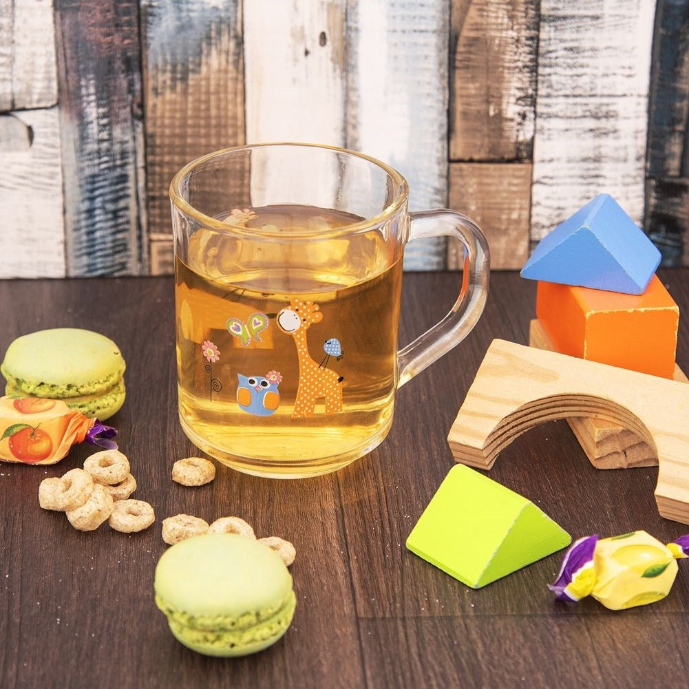 Un vaso de té con pegatinas de jirafa y búho, junto a macarons, galletas y juguetes de madera.
