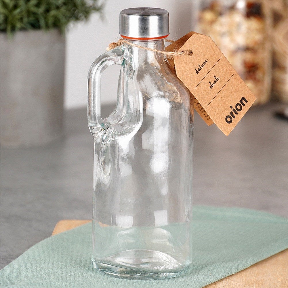 Una botella de vidrio transparente con asa, tapa plateada y etiqueta marrón.