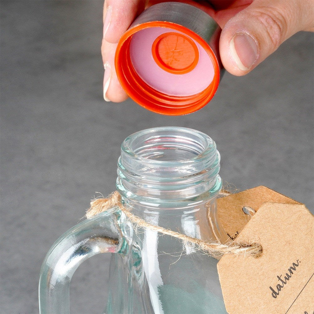 Una mano sostiene una tapa naranja sobre una botella de vidrio.