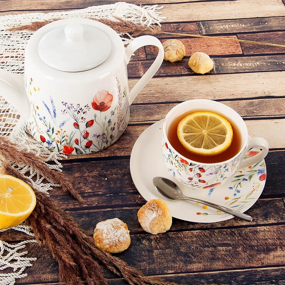 Una tetera y taza floral con limón y galletas sobre una mesa de madera.