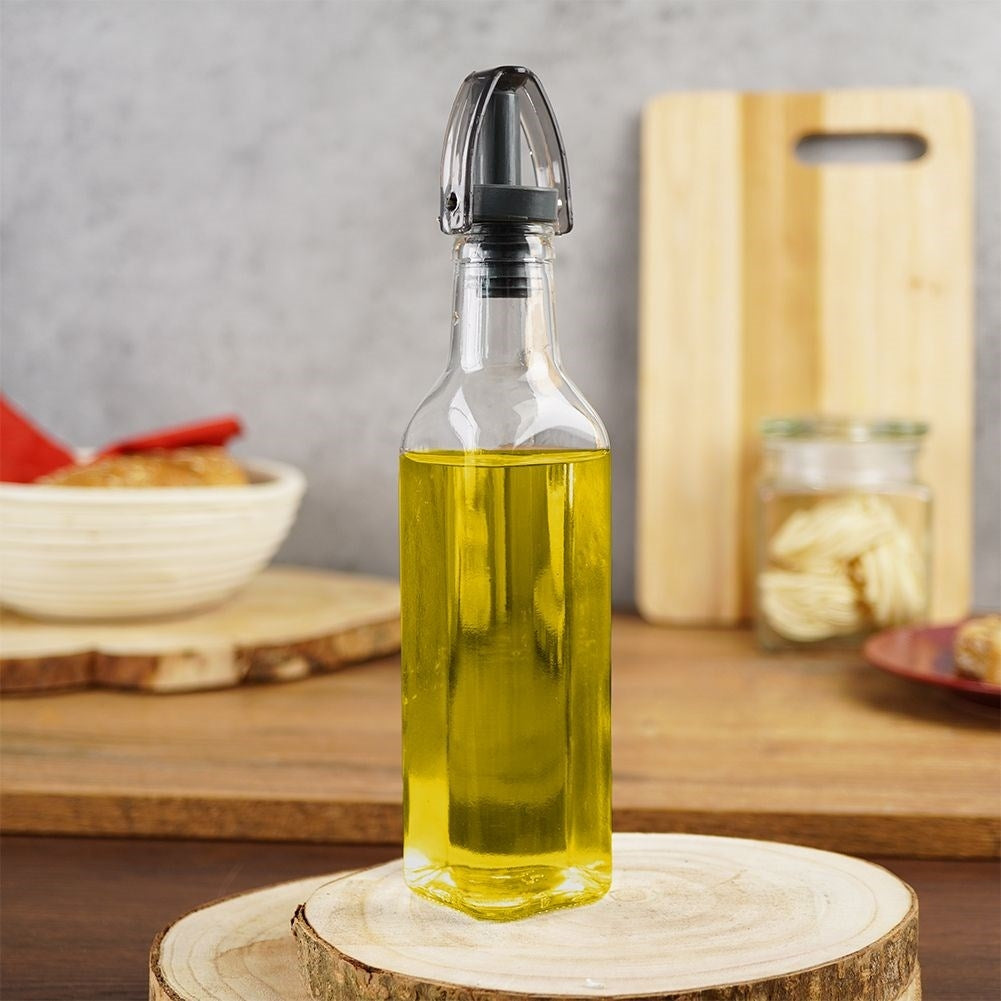 Botella de vidrio con aceite de oliva sobre rodaja de madera, bol y tabla de cortar al fondo.