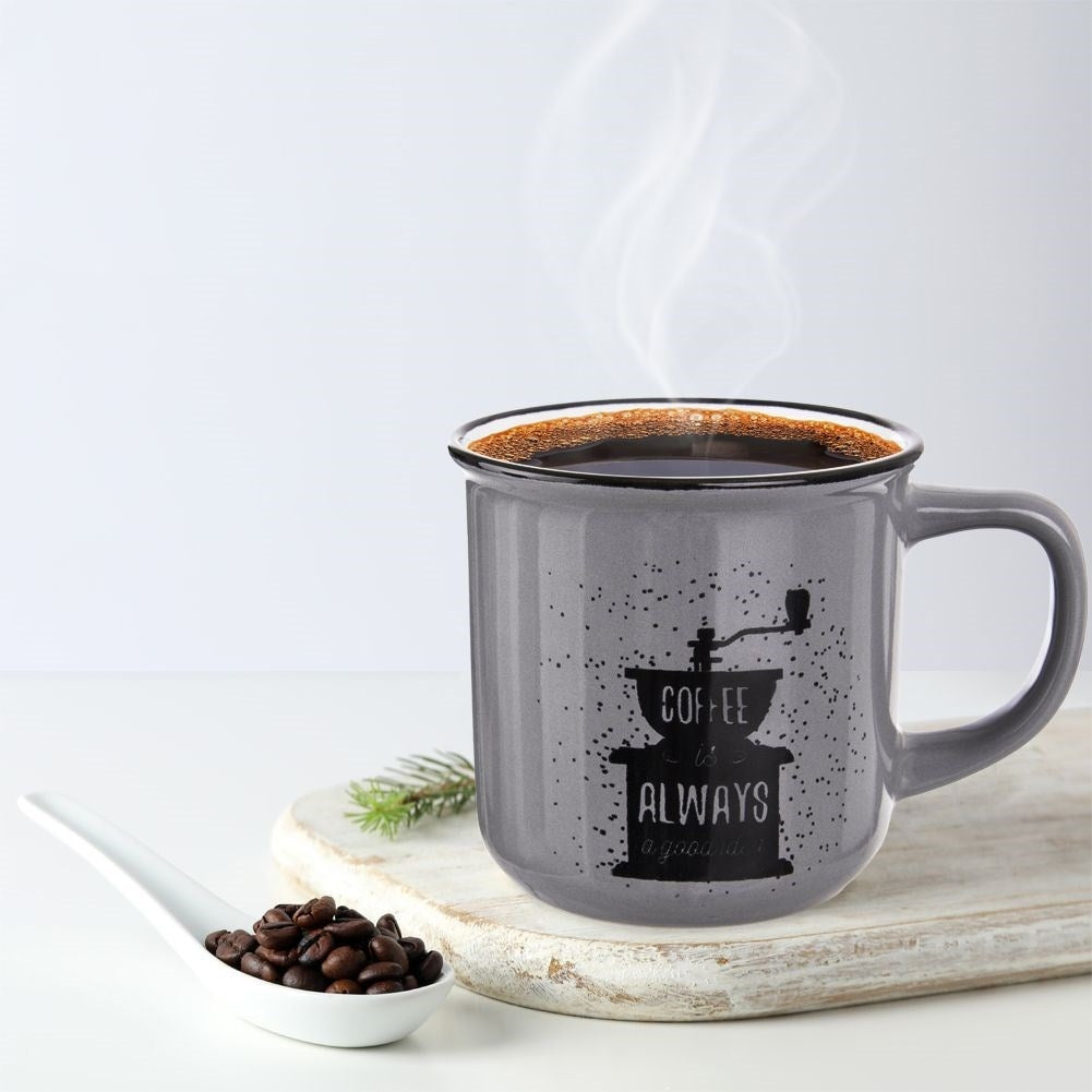 Una taza gris de café humeante con granos de café y ramita de pino.