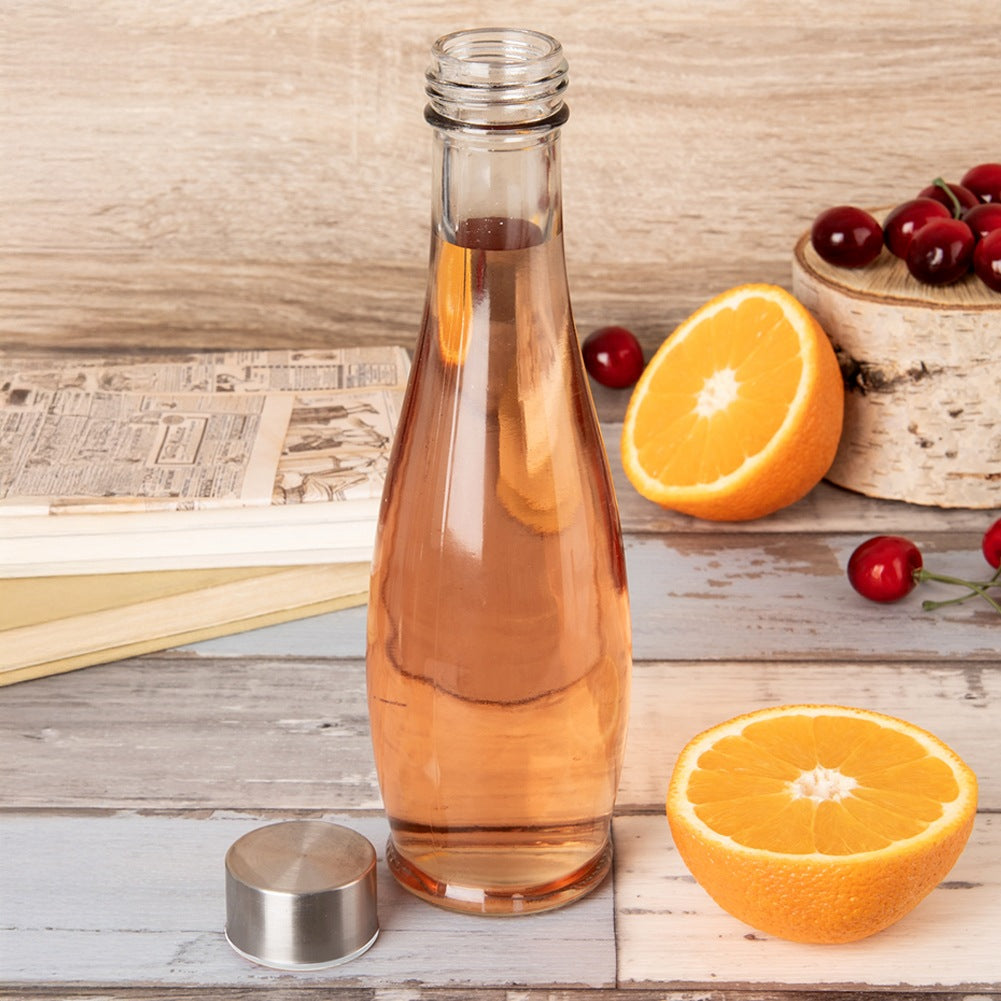 Una botella de vidrio con bebida rosa junto a naranjas y cerezas.
