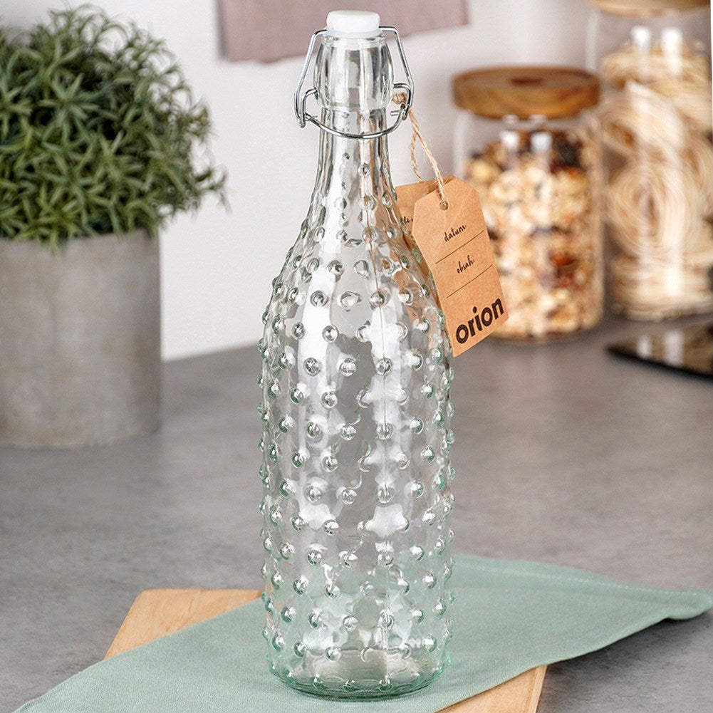 Una botella de vidrio transparente con patrón de puntos en relieve y tapa abatible.