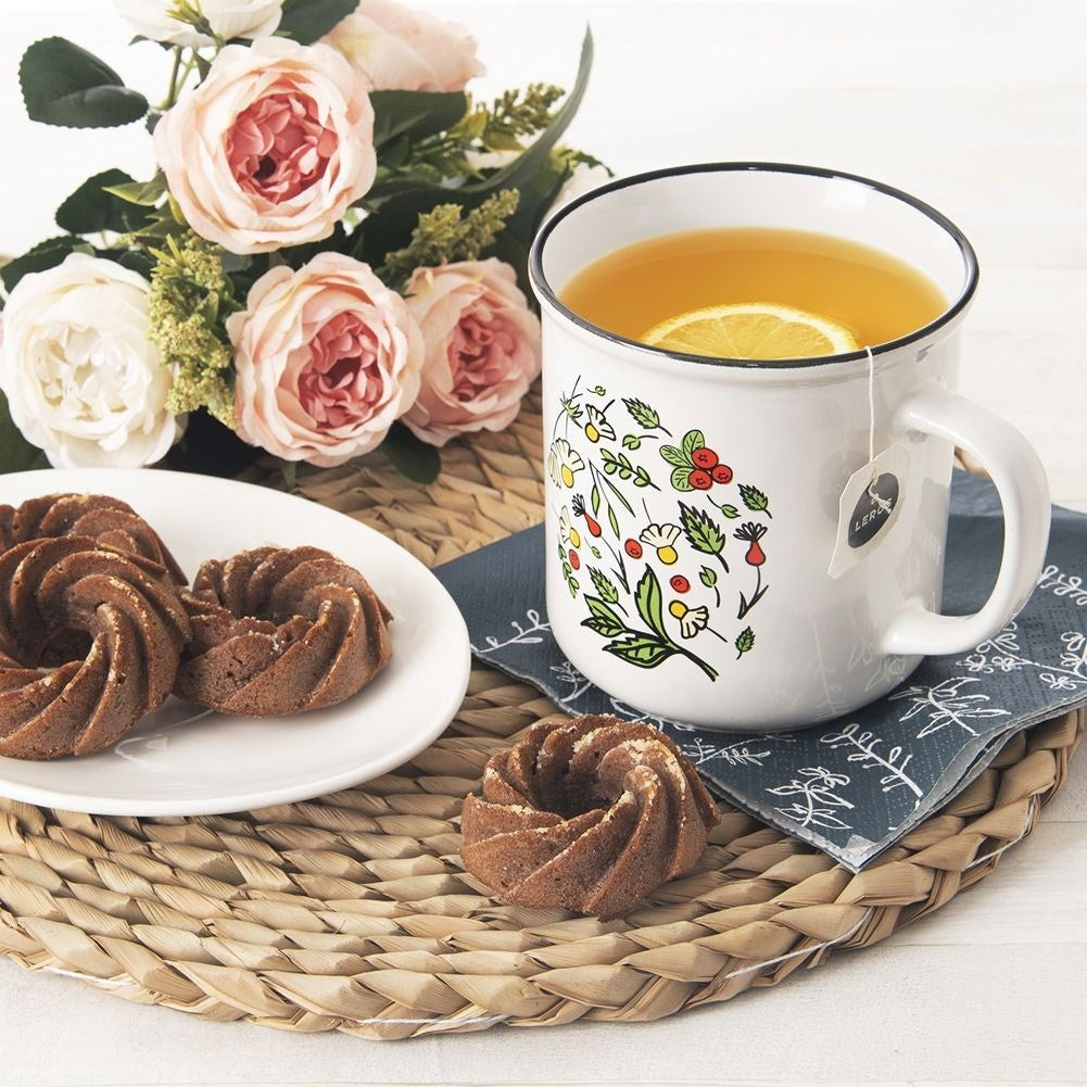 Una taza de té con limón, pasteles y flores sobre un mantel individual.
