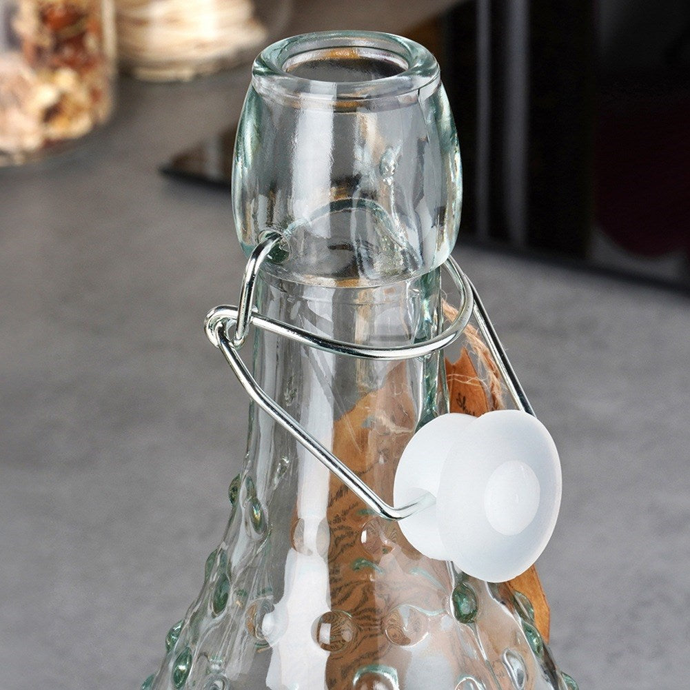 Primer plano del cuello de una botella de vidrio con tapa abatible y tapón de goma blanco.