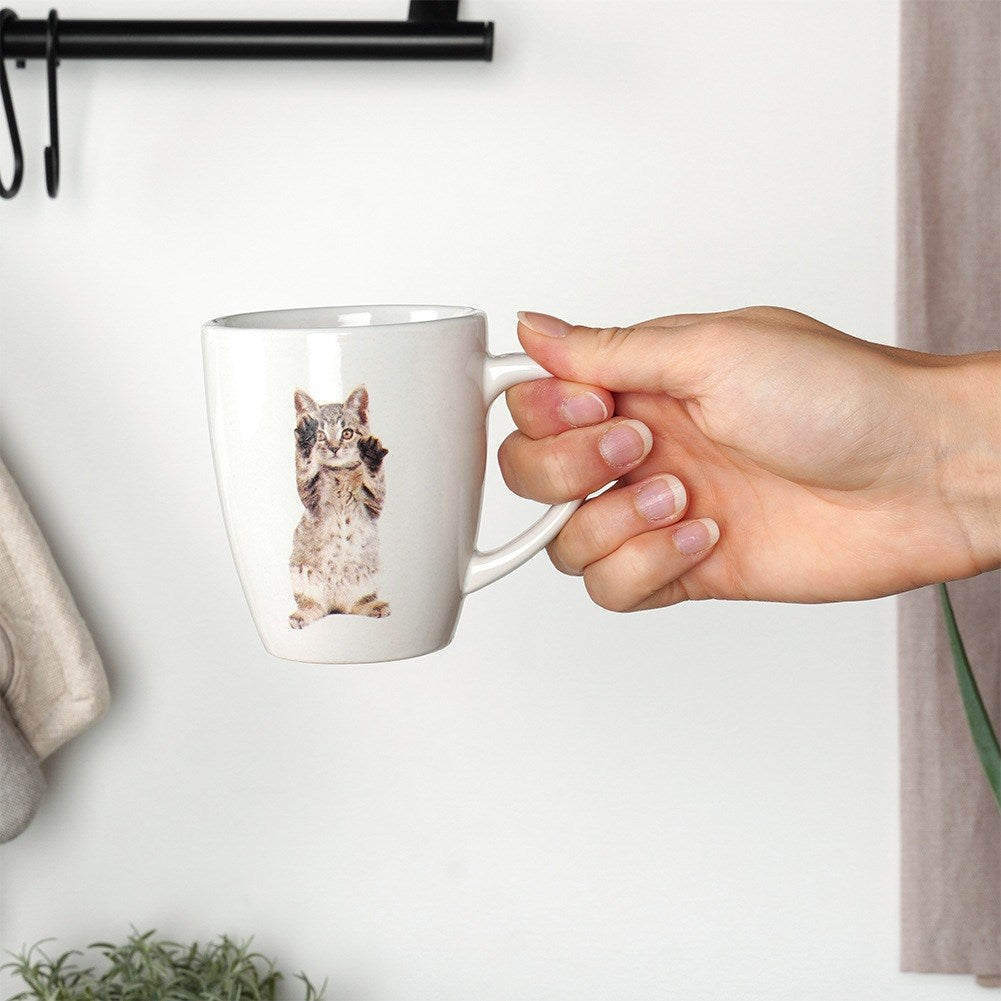 Una mano sostiene una taza blanca con un lindo gráfico de gatito.