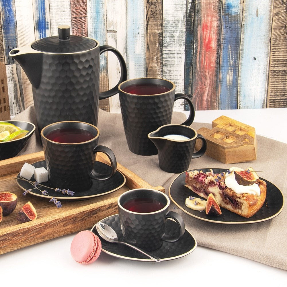 Juego de té negro con textura de panal, tazas, tetera, jarra de leche, pastel, higos y macarons.