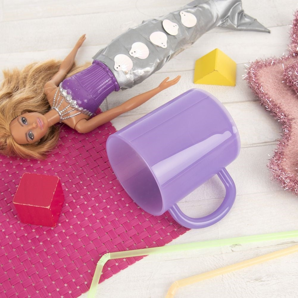 Una muñeca Barbie con cola de sirena yace junto a una taza morada.