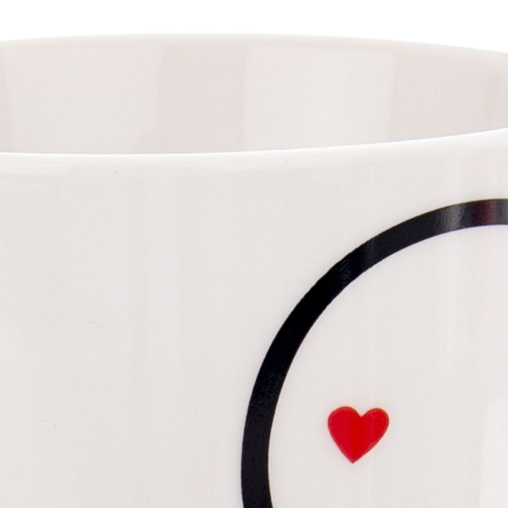 Una taza blanca con un círculo negro y un pequeño corazón rojo.