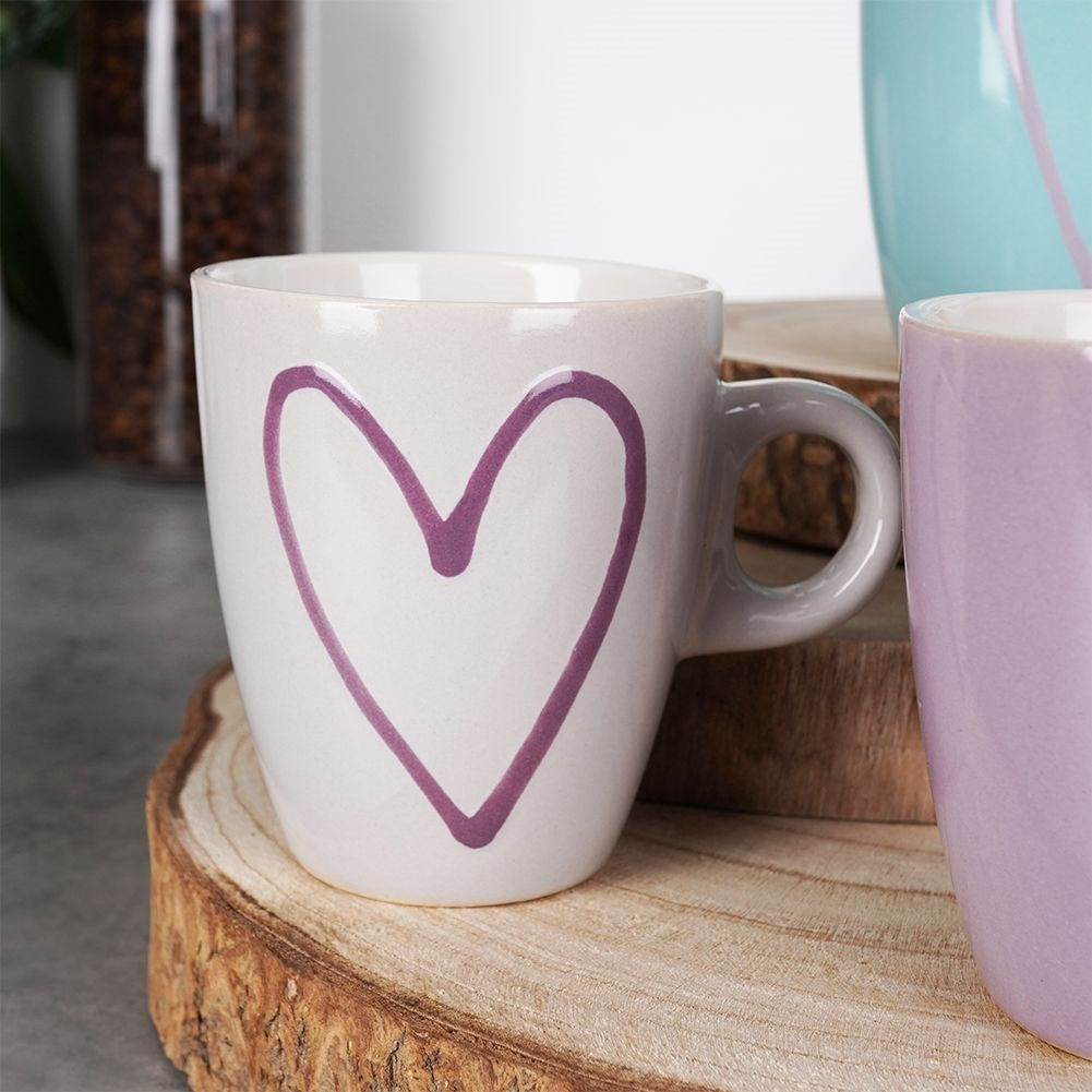 Una taza blanca con un corazón morado y dos tazas más al lado.