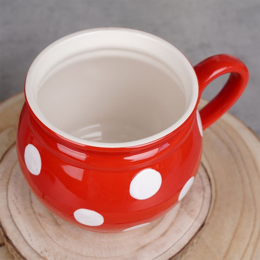 Una taza de cerámica roja con lunares blancos y un asa.