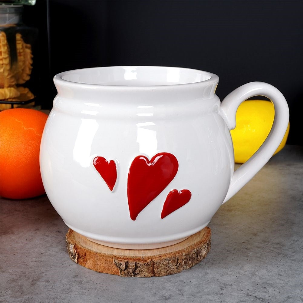 Taza de cerámica blanca con corazones rojos sobre un posavasos de rodaja de madera.