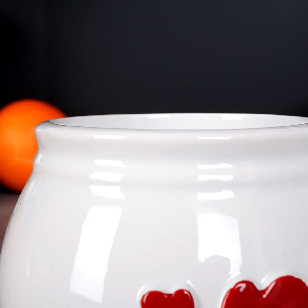 Cuenco blanco de cerámica con corazones rojos, bola naranja al fondo.