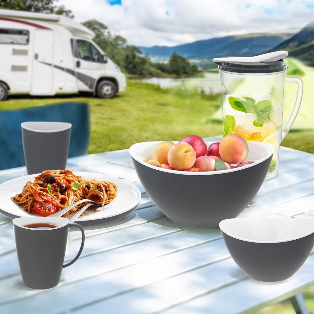 Una autocaravana junto a un lago con una mesa puesta con comida y fruta.