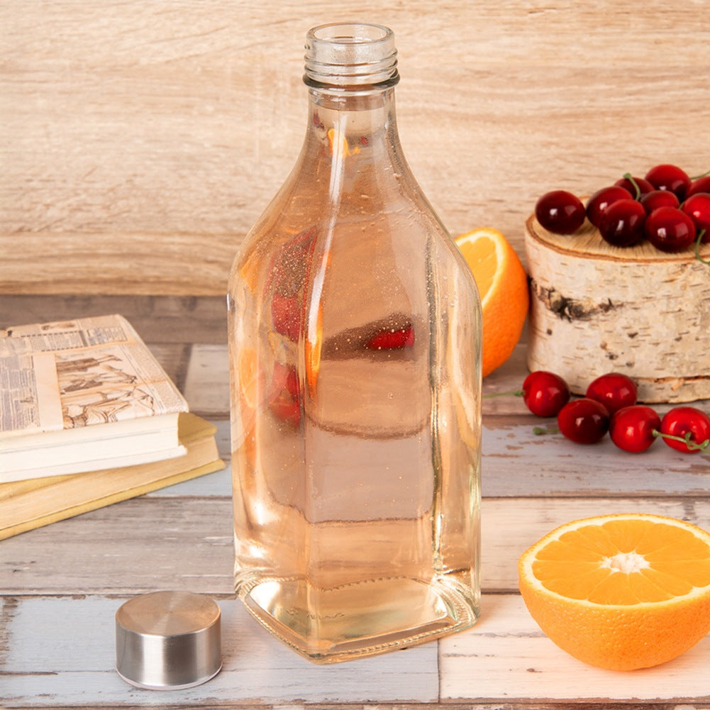Una botella de vidrio con líquido claro junto a libros y frutas.