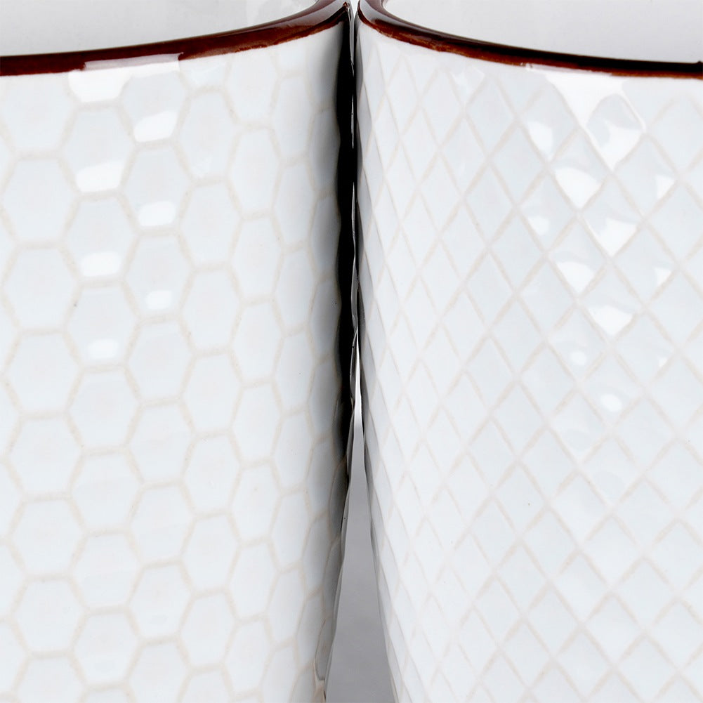 Dos tazas blancas con borde marrón, una con patrón de panal, la otra con patrón de diamantes.