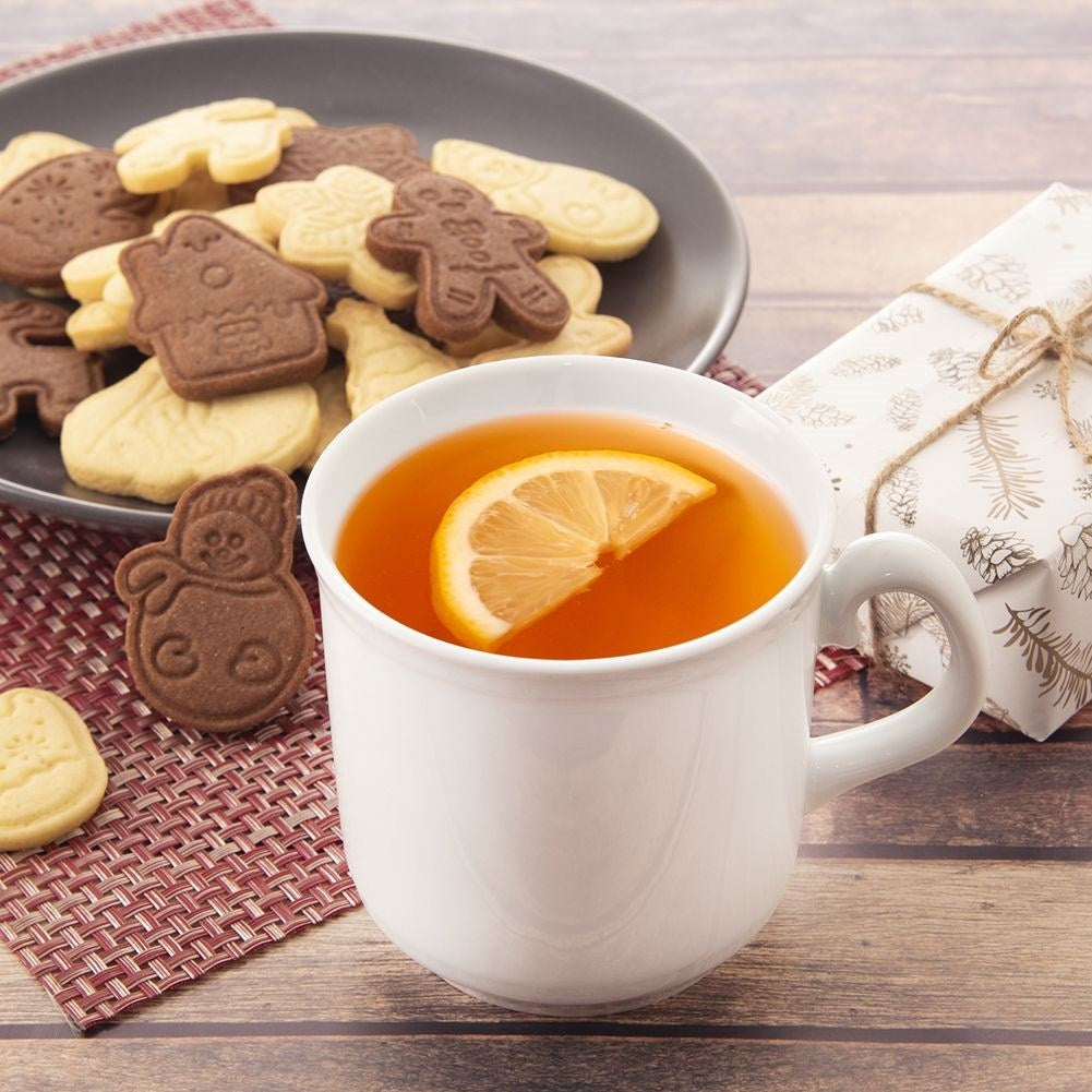 Una taza blanca de té con limón, galletas y un regalo al lado.