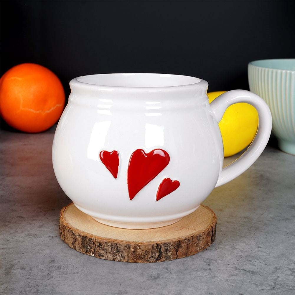 Taza blanca con corazones rojos sobre posavasos de madera, naranja y limón al lado.
