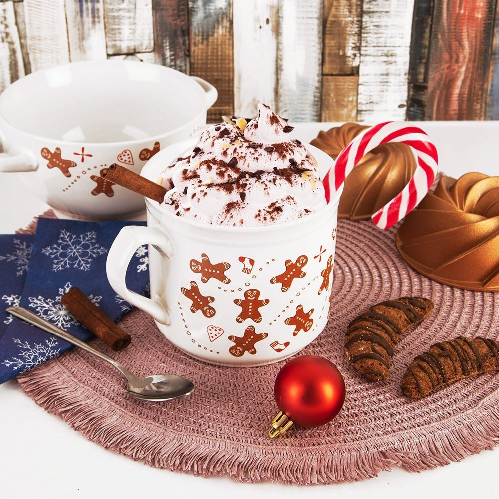 Una taza de chocolate caliente con crema y canela, cerca de galletas y bastones de caramelo.