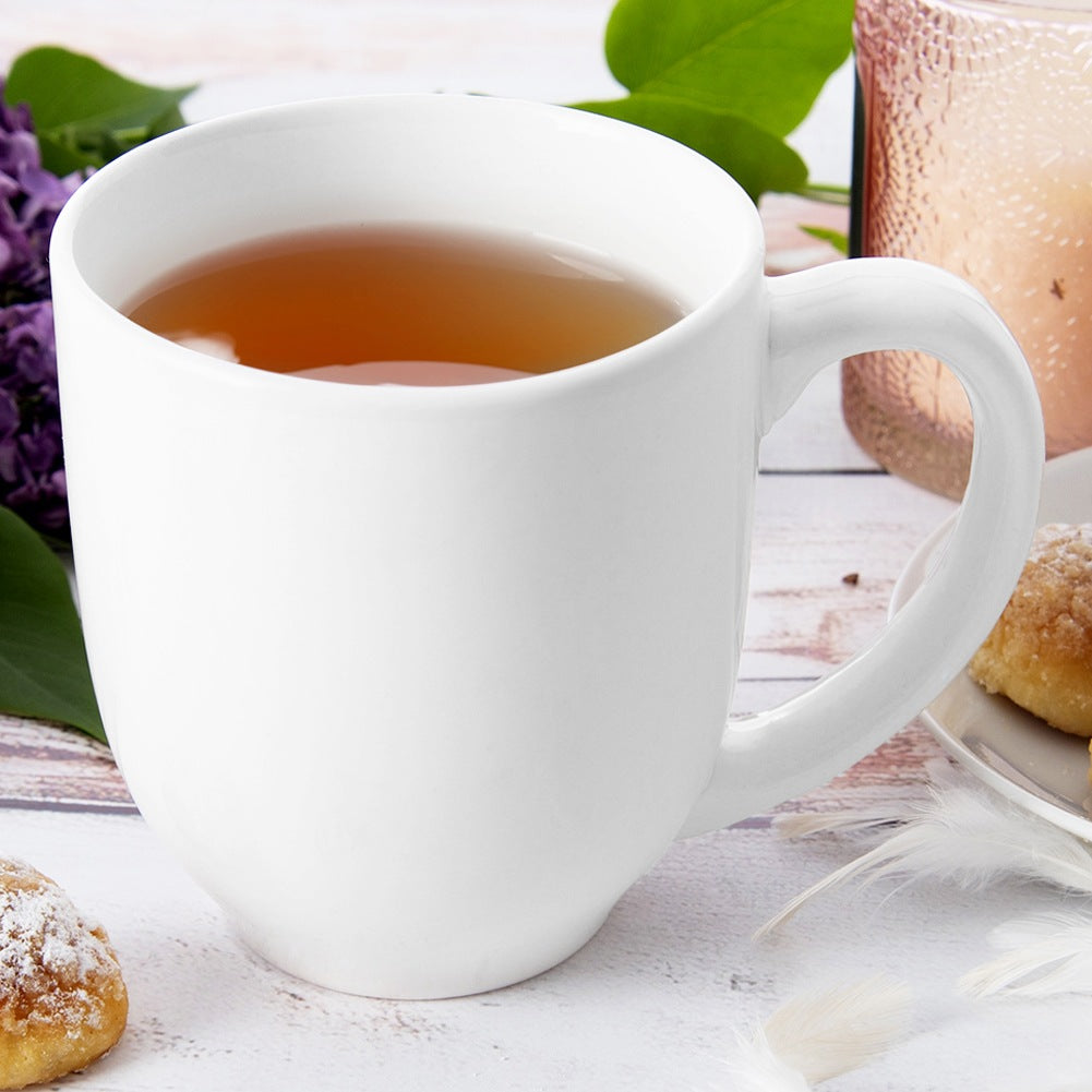 Una taza blanca de té sobre mesa de madera con pasteles y flores.