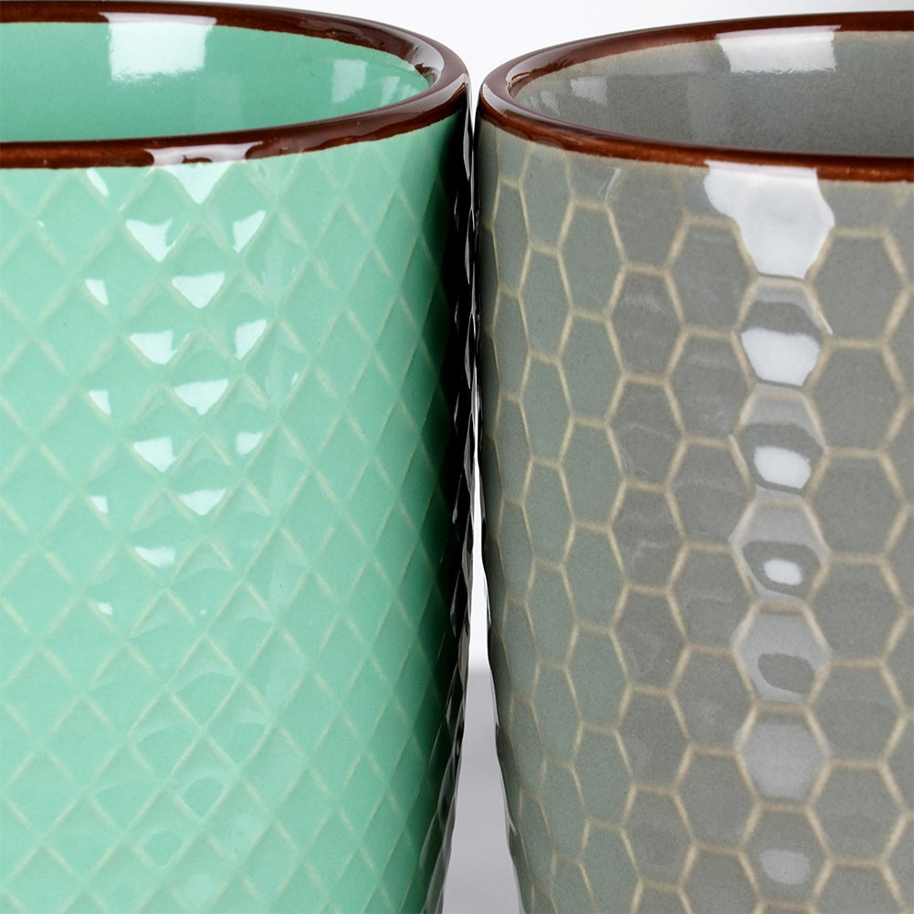 Dos tazas: una verde menta con rombos, una gris con panal de abeja.