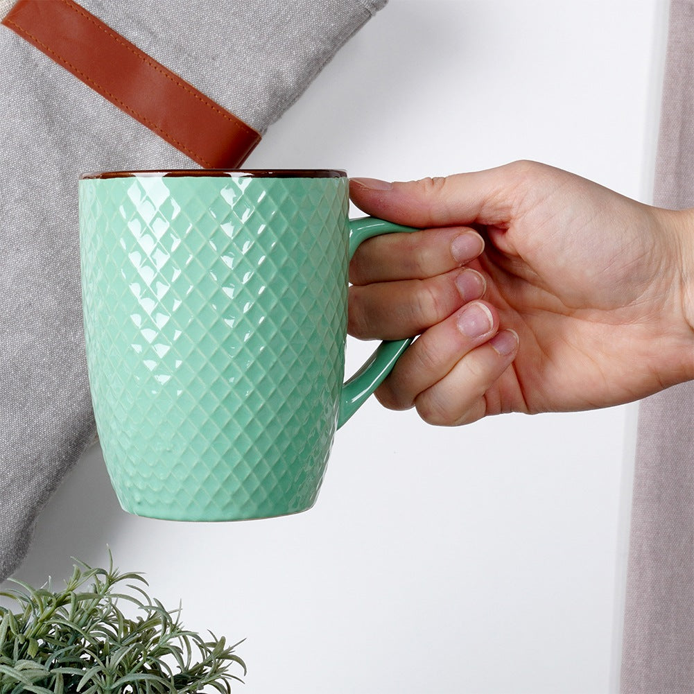Una mano sostiene una taza verde texturizada con borde marrón.