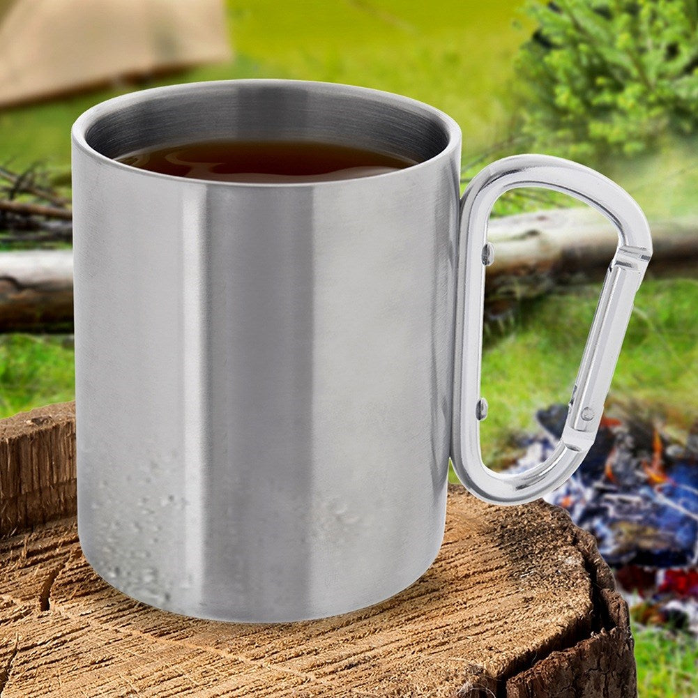 Taza de metal con café sobre tocón de árbol, fogata y tienda de campaña al fondo.