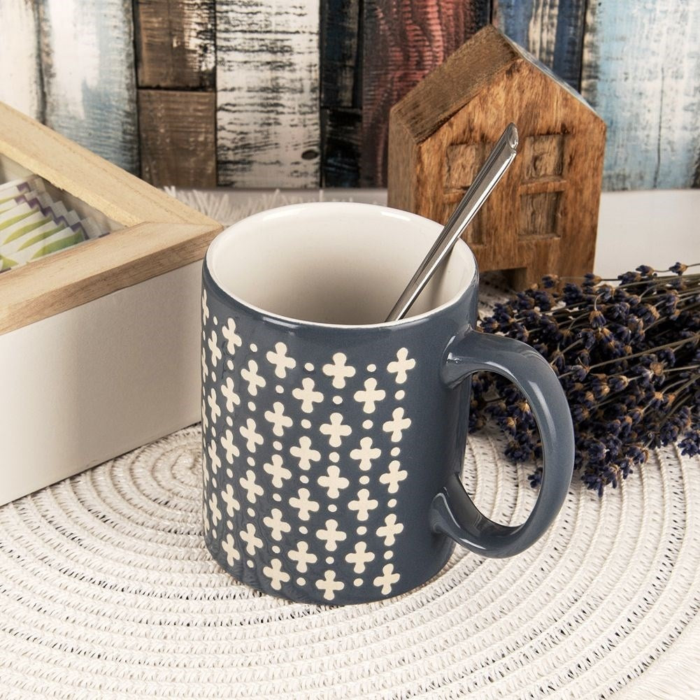 Taza gris con patrón blanco, cuchara, casita de madera, lavanda.